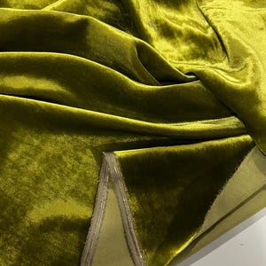 May include: Close-up of a folded piece of olive green velvet fabric with a gold trim. The fabric is soft and luxurious, with a subtle sheen.