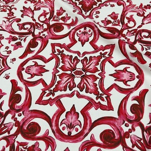 May include: White fabric with a repeating pattern of red and pink floral designs. The pattern is reminiscent of a traditional Italian tile design.