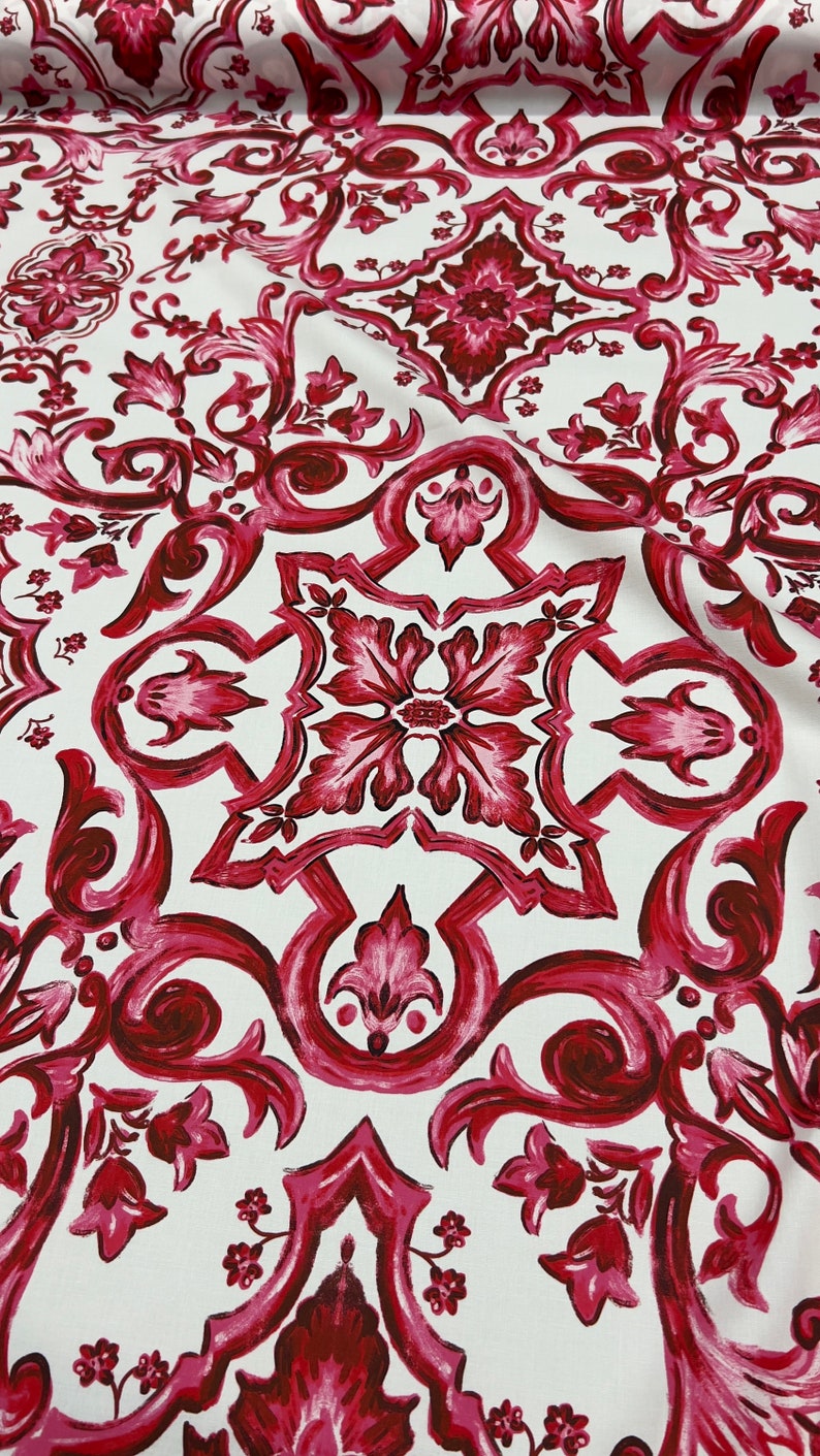 May include: White fabric with a repeating pattern of red and pink floral designs. The pattern is reminiscent of a traditional Italian tile design.