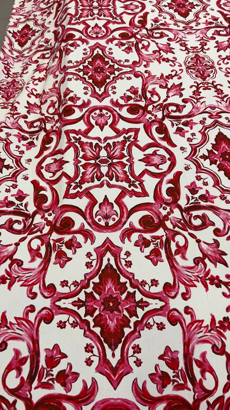 May include: White fabric with a repeating pattern of red and pink floral designs. The pattern is intricate and features a damask-like design.