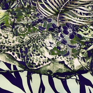 Op de afbeelding: Stof met een jungle-thema. De stof heeft een luipaard, palmbladeren en bloempatronen in groen, wit en marineblauw. De onderkant van de stof heeft een zebra- en giraffenprint.