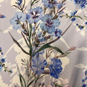 May include: A close-up of a light purple fabric with a floral print. The flowers are blue and white with green stems and leaves.