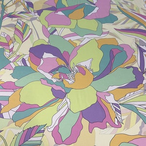 Puede incluir: Una tela floral con un patrón repetitivo de grandes rosas estilizadas en tonos de morado, verde, amarillo y rosa sobre un fondo crema.