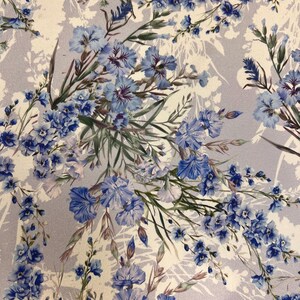 May include: A light gray fabric with a floral pattern featuring blue flowers and green leaves. The flowers are arranged in a random pattern and are of varying sizes.
