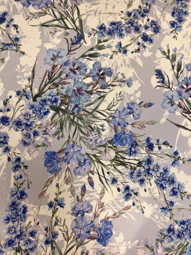 May include: A light gray fabric with a floral pattern featuring blue flowers and green leaves. The flowers are arranged in a random pattern and are of varying sizes.