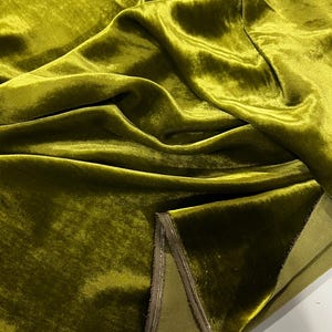 May include: Close-up of a folded piece of olive green velvet fabric with a light brown trim. The fabric has a soft, plush texture.