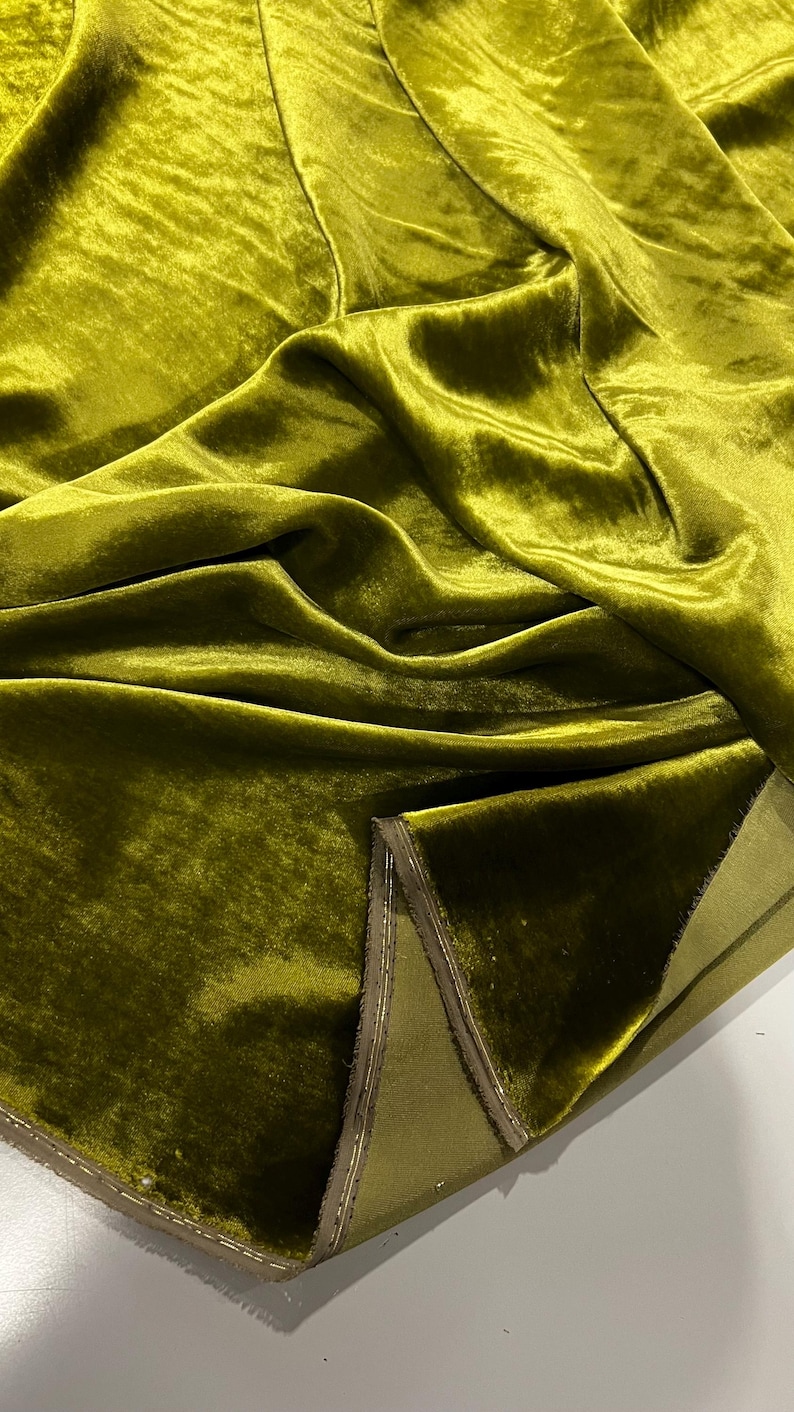May include: Close-up of a folded piece of olive green velvet fabric with a light brown trim. The fabric has a soft, plush texture.