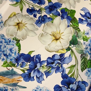 May include: A fabric with a floral design. It features white and blue flowers, including hydrangeas and other blooms, with green leaves and a small bird. The design is set against a white background, creating a vibrant and detailed print.