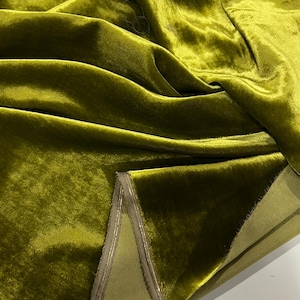 May include: Close-up of a folded piece of olive green velvet fabric with a gold trim. The fabric is soft and luxurious, with a subtle sheen.