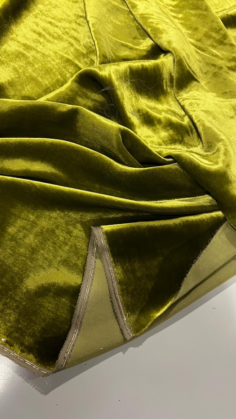 May include: Close-up of a folded piece of olive green velvet fabric with a gold trim. The fabric is soft and luxurious, with a subtle sheen.