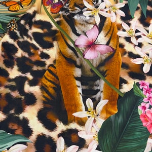 K&ouml;nnte beinhalten: Ein Tiger mit orangefarbenen und schwarzen Streifen sitzt in einer Dschungelkulisse mit wei&szlig;en Bl&uuml;ten, gr&uuml;nen Bl&auml;ttern und Schmetterlingen. Der Tiger ist von einem Leopardenmuster umgeben.