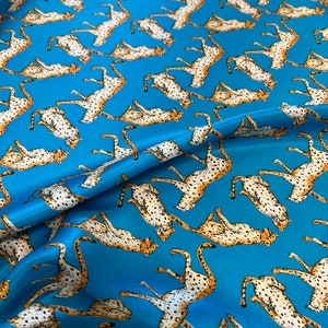 May include: Blue fabric with a repeating pattern of brown and white cheetahs. The fabric is folded in the centre.