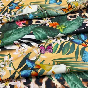 K&ouml;nnte beinhalten: Ein gelber Stoff mit tropischem Druck, der schwarze Panther, Zebras, Schmetterlinge und Blumen zeigt. Der Stoff ist gefaltet, um einen Tigerdruck auf der unteren Schicht zu zeigen.