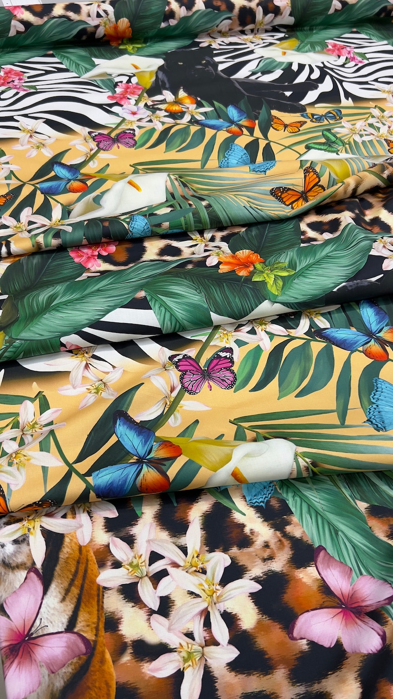 K&ouml;nnte beinhalten: Ein gelber Stoff mit tropischem Druck, der schwarze Panther, Zebras, Schmetterlinge und Blumen zeigt. Der Stoff ist gefaltet, um einen Tigerdruck auf der unteren Schicht zu zeigen.
