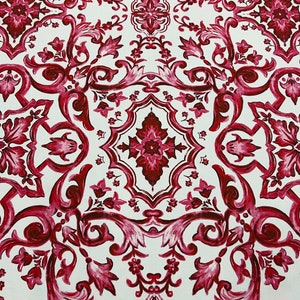 May include: A white fabric with a repeating pattern of burgundy floral designs. The pattern is symmetrical and features intricate details.