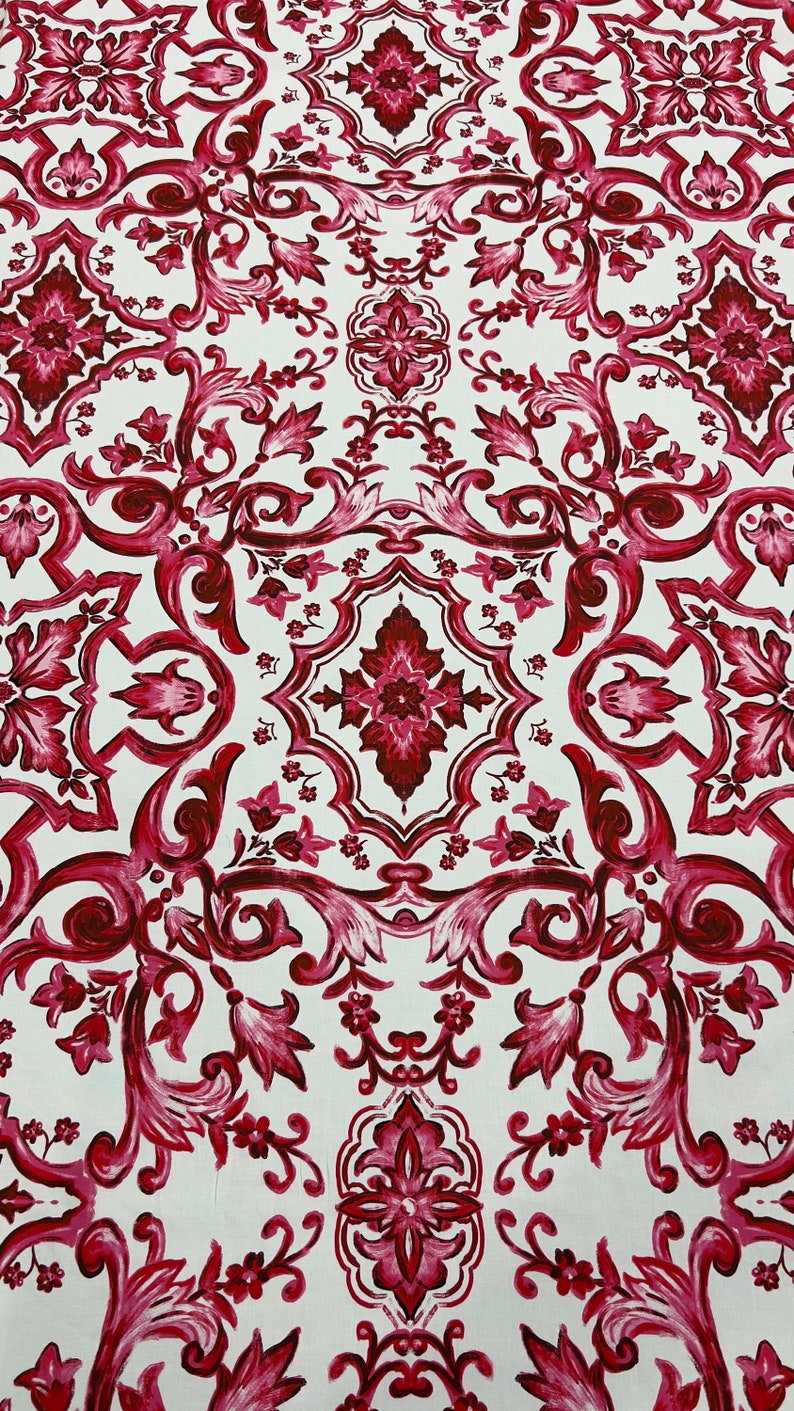 May include: A white fabric with a repeating pattern of burgundy floral designs. The pattern is symmetrical and features intricate details.