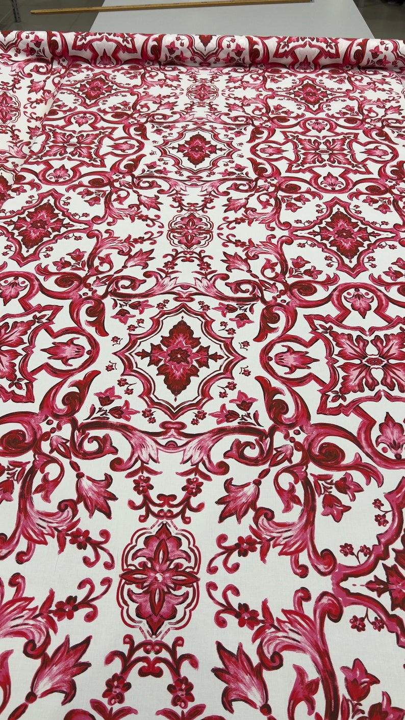 May include: White fabric with a repeating pattern of red and pink floral designs. The pattern resembles a traditional tile design.