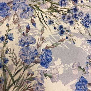 May include: A white fabric with a blue floral pattern. The flowers are a variety of shapes and sizes, and they are arranged in a random pattern. The fabric has a subtle shimmer.