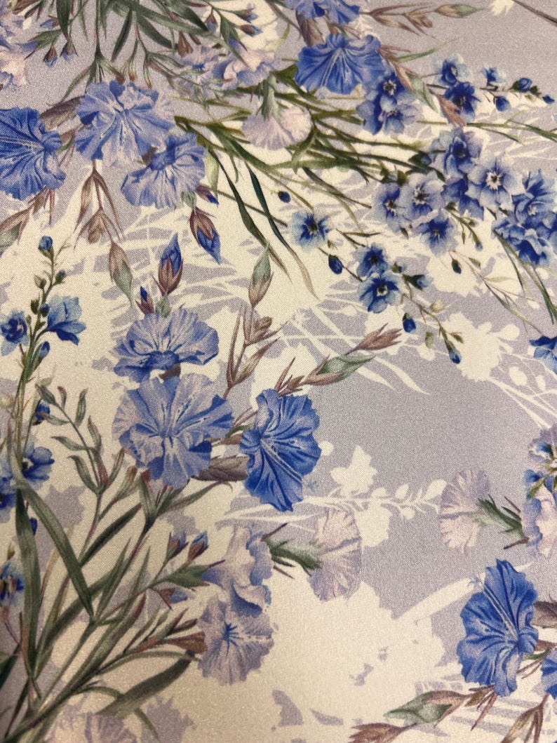 May include: A white fabric with a blue floral pattern. The flowers are a variety of shapes and sizes, and they are arranged in a random pattern. The fabric has a subtle shimmer.
