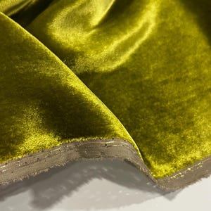 May include: A close-up of a bright green velvet fabric with a subtle sheen. The fabric has a decorative trim along the edge.