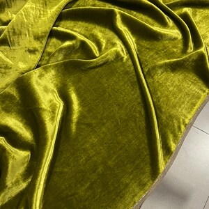 May include: A close-up of a smooth, green velvet fabric. The fabric is folded and draped, showing its texture and sheen.