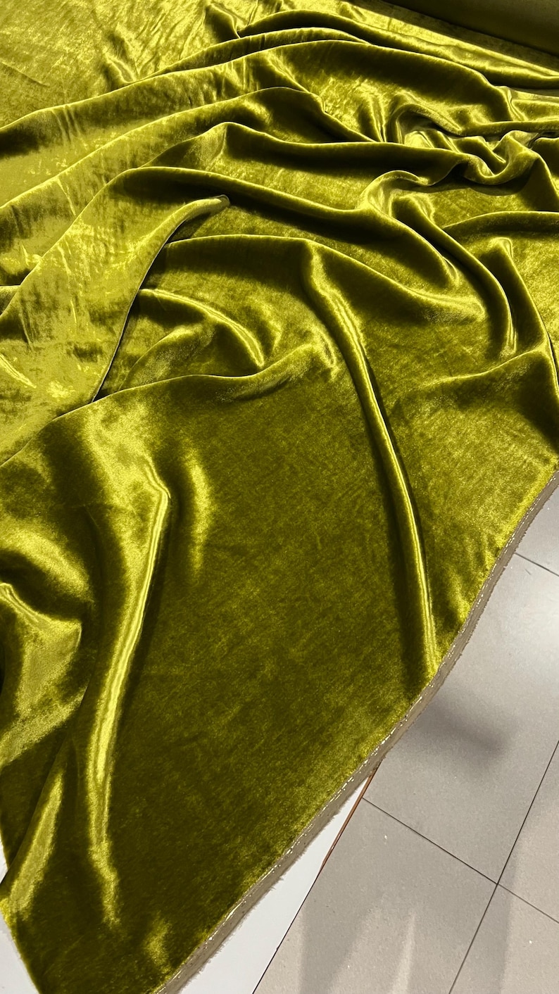May include: A close-up of a smooth, green velvet fabric. The fabric is folded and draped, showing its texture and sheen.
