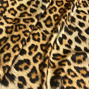 May include: Close-up of a brown and black leopard print fabric. The fabric has a silky texture and is ideal for sewing projects.