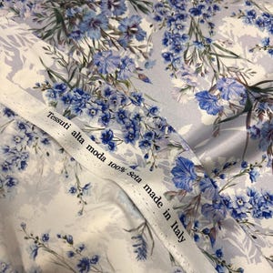 May include: White fabric with a blue floral pattern. The fabric has a label that reads "Tessuti alta moda 100% seta made in Italy".