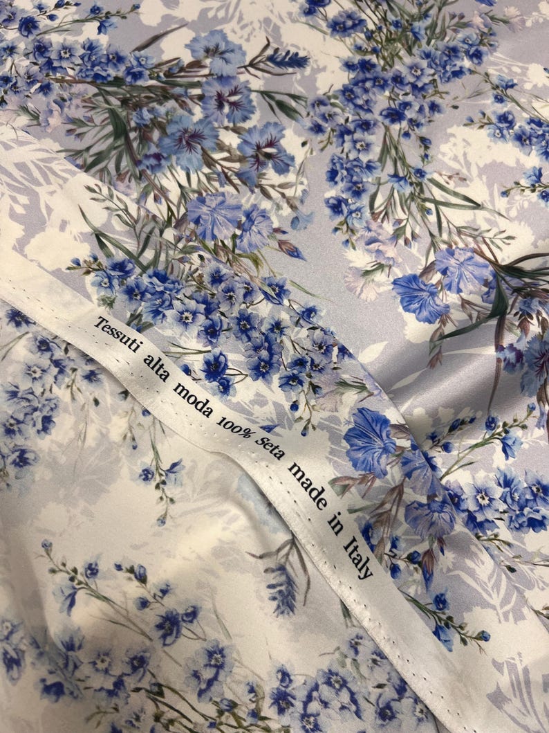 May include: White fabric with a blue floral pattern. The fabric has a label that reads "Tessuti alta moda 100% seta made in Italy".