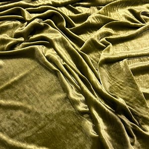 May include: A close-up of a soft, green velvet fabric. The fabric is draped and folded, showing its texture and sheen.