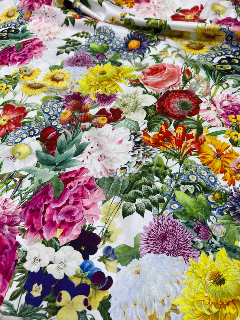 May include: A white fabric with a floral print featuring a variety of flowers in shades of pink, red, yellow, blue, and white. The flowers are arranged in a random pattern and appear to be realistic.