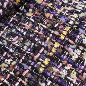 Könnte beinhalten: Nahaufnahme eines strukturierten Stoffes mit einem gewebten Muster. Der Stoff weist eine Mischung aus Farben auf, darunter Schwarz, Lila, Rosa, Gold und Weiß. Das Gewebe enthält dekoratives Goldgarn und eine Vielzahl von Texturen.