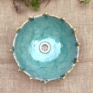 May include: A turquoise ceramic sink with a scalloped edge and a silver drain.