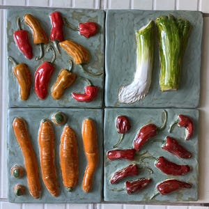 Puede incluir: Cuatro baldosas de cerámica cuadradas con imágenes en relieve de verduras. Las baldosas presentan pimientos rojos y naranjas, zanahorias y un puerro. Las verduras están sobre un fondo azul verdoso claro.