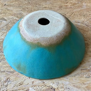 May include: A turquoise ceramic bowl with a white rim and a small hole in the center. The bowl has a rustic, handmade look.