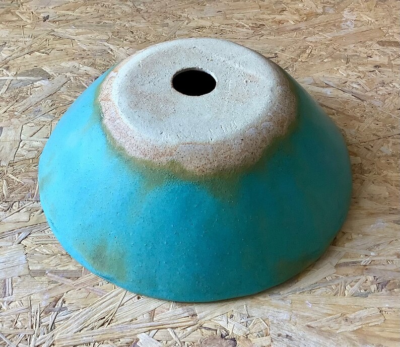 May include: A turquoise ceramic bowl with a white rim and a small hole in the center. The bowl has a rustic, handmade look.