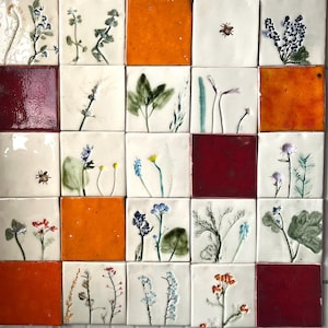 May include: A grid of square ceramic tiles, each decorated with botanical motifs. The tiles display hand-painted images of flowers, leaves, and insects. Some tiles are solid orange or burgundy, creating a varied pattern.