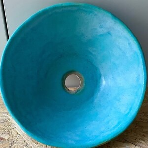 May include: A turquoise ceramic sink with a round shape and a hole in the center for the drain.