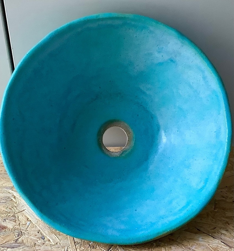 May include: A turquoise ceramic sink with a round shape and a hole in the center for the drain.