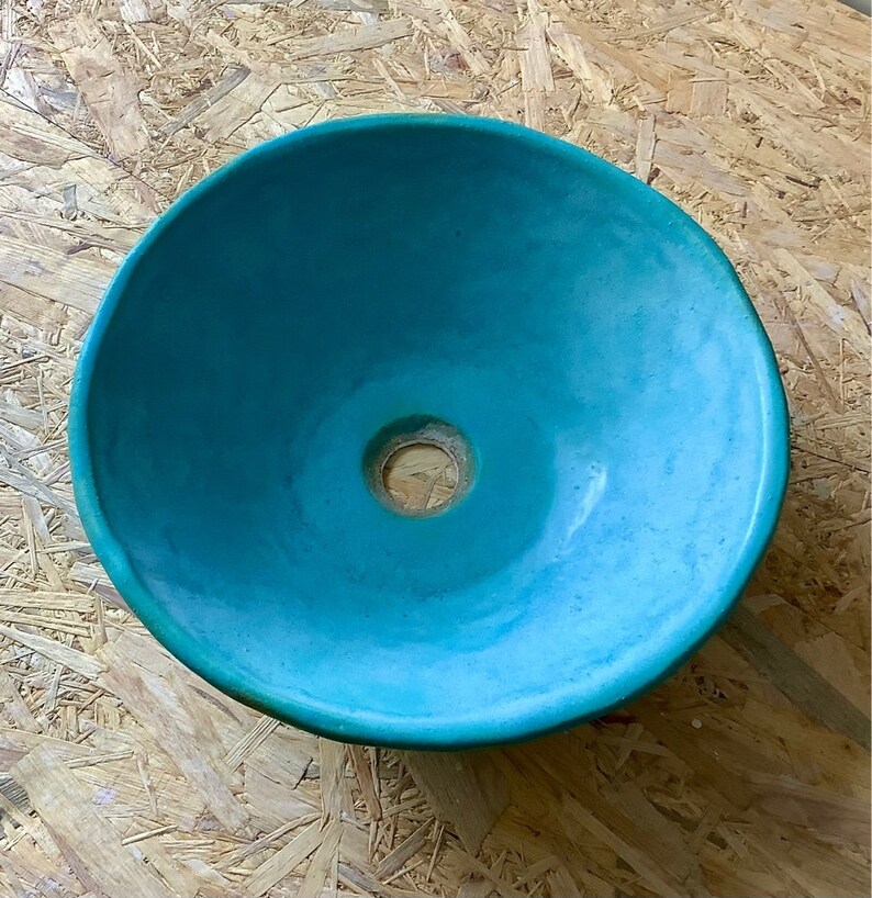 May include: A turquoise blue ceramic sink bowl with a round shape and a small drain hole in the center.