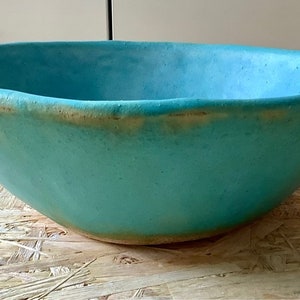 May include: A large, turquoise ceramic bowl with a slightly uneven rim. The bowl has a subtle, speckled texture and a slightly lighter rim.
