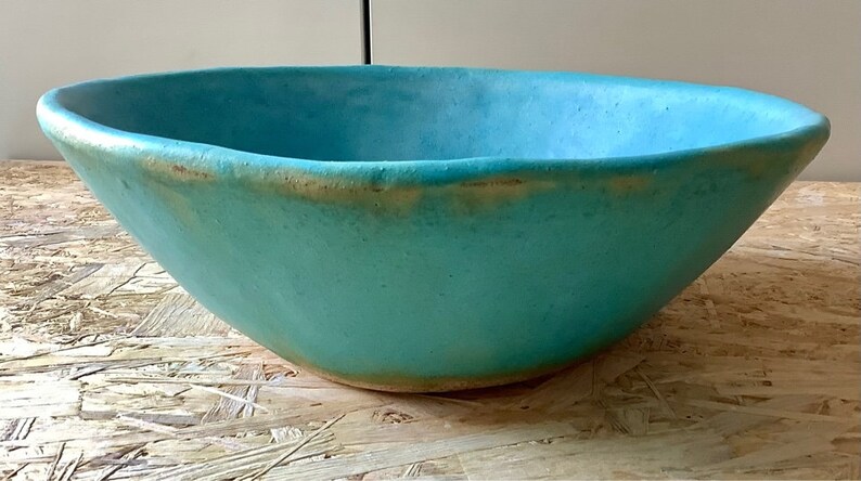 May include: A large, turquoise ceramic bowl with a slightly uneven rim. The bowl has a subtle, speckled texture and a slightly lighter rim.