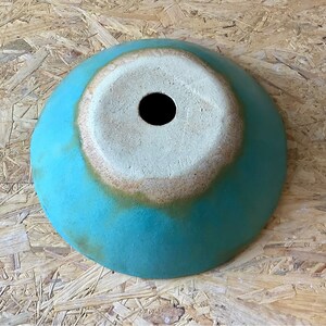 May include: A turquoise ceramic bowl with a white glazed interior and a small hole in the center. The bowl has a rustic, handmade look.