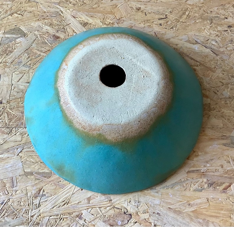 May include: A turquoise ceramic bowl with a white glazed interior and a small hole in the center. The bowl has a rustic, handmade look.
