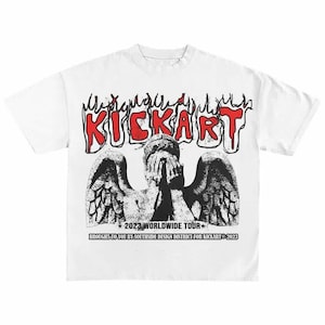 Könnte beinhalten: Weißes T-Shirt mit einem verwitterten Grafikdesign. Das Design zeigt das Wort "KICKART" in Rot, stilisierte Flammen und ein Schwarz-Weiß-Bild einer Statue mit Flügeln. Der Text "2023 WORLDWIDE TOUR" ist ebenfalls enthalten.