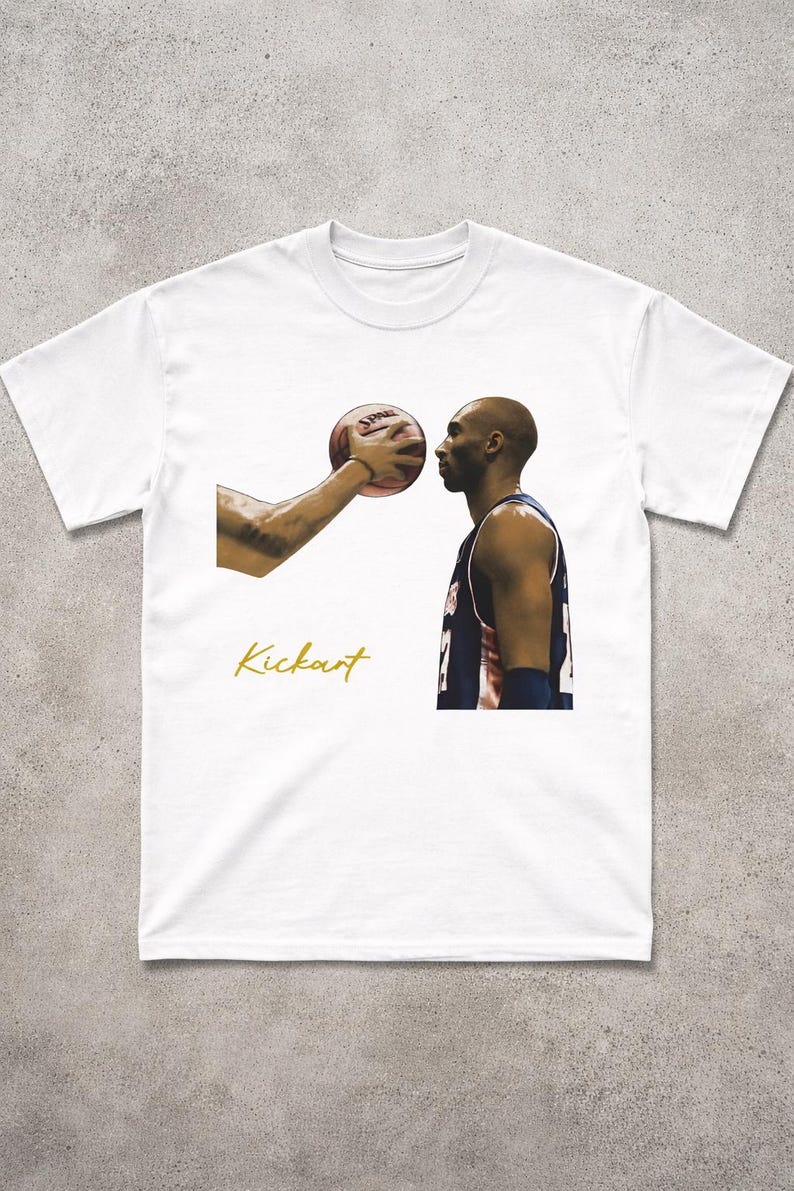 May include: White t-shirt with a basketball player and a basketball. The image includes the word "Kickart" in gold script. The basketball is held near the player's face.