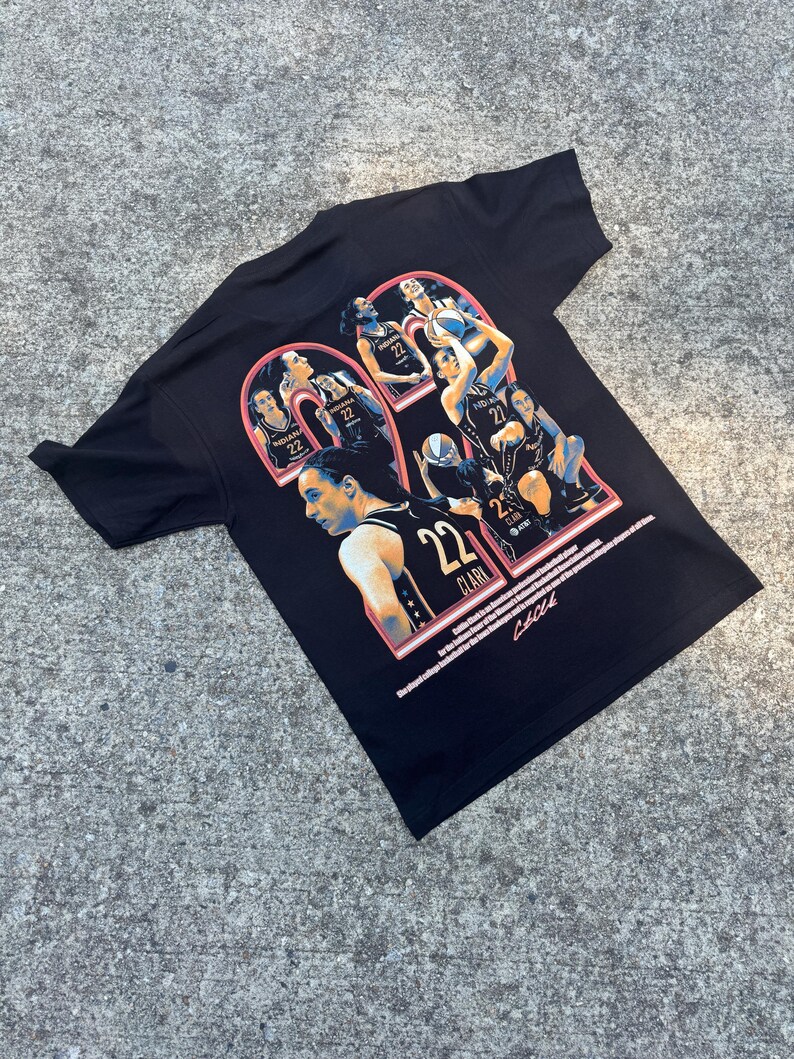 May include: Black t-shirt with a graphic print of basketball players in a collage style. The players are wearing orange and blue uniforms. The number "22" is prominently displayed in red and orange. The text "CLARK" is also visible on the shirt.