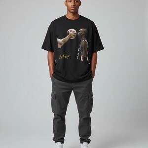 May include: Black t-shirt with a basketball graphic and the word "Kickart" in gold script. The person in the image is wearing dark grey cargo trousers and white trainers. The image depicts a basketball player and a basketball.