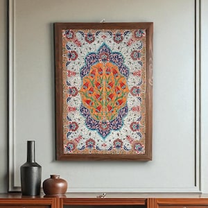 Könnte beinhalten: Gerahmtes Wandkunstwerk mit detailliertem floralem Design. Das Kunstwerk zeigt ein zentrales orangefarbenes Motiv mit roten Blumen, umgeben von einem blau-weißen gemusterten Rand, alles in einem Holzrahmen. Das Stück hängt an einer hellgrauen Wand.