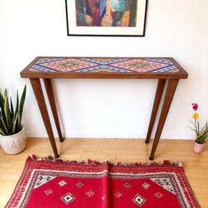 May include: A wooden console table with a colorful geometric patterned top and dark brown legs. The table is sitting on a red rug with a geometric pattern.